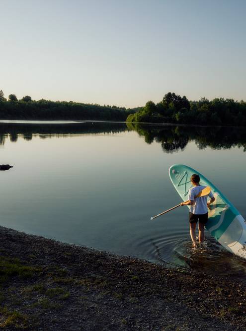Mann trägt ein SUP in den Bütgenbacher See